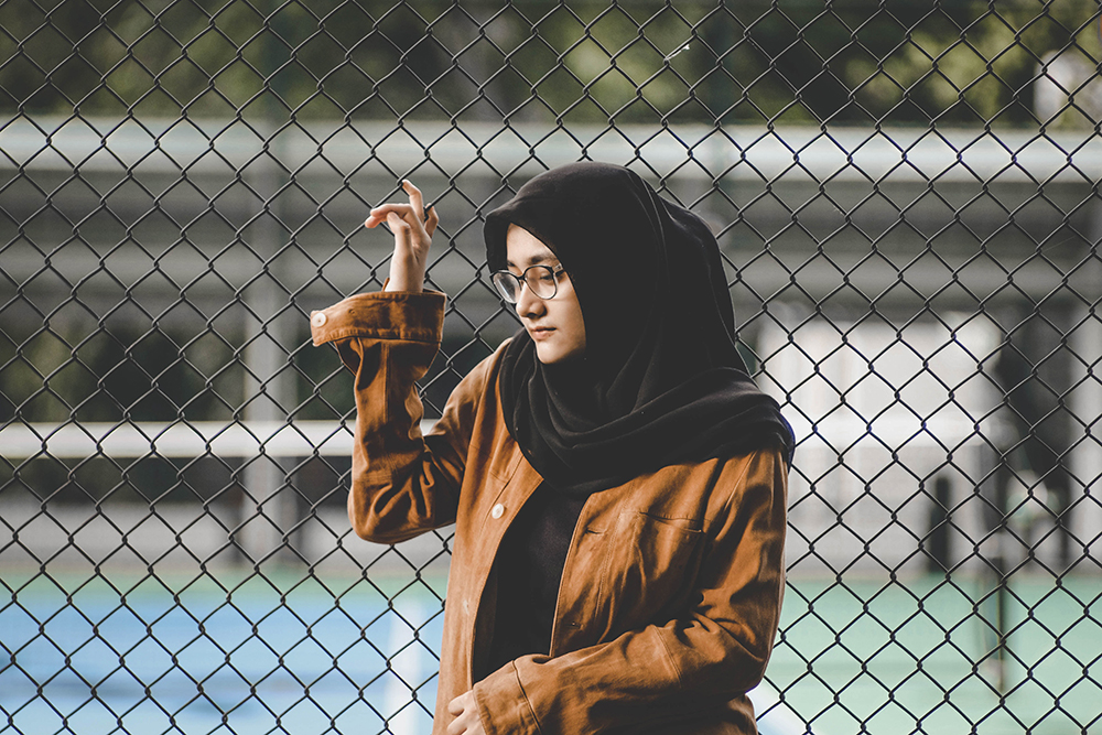 girl leaning on a fence in a brown jacket